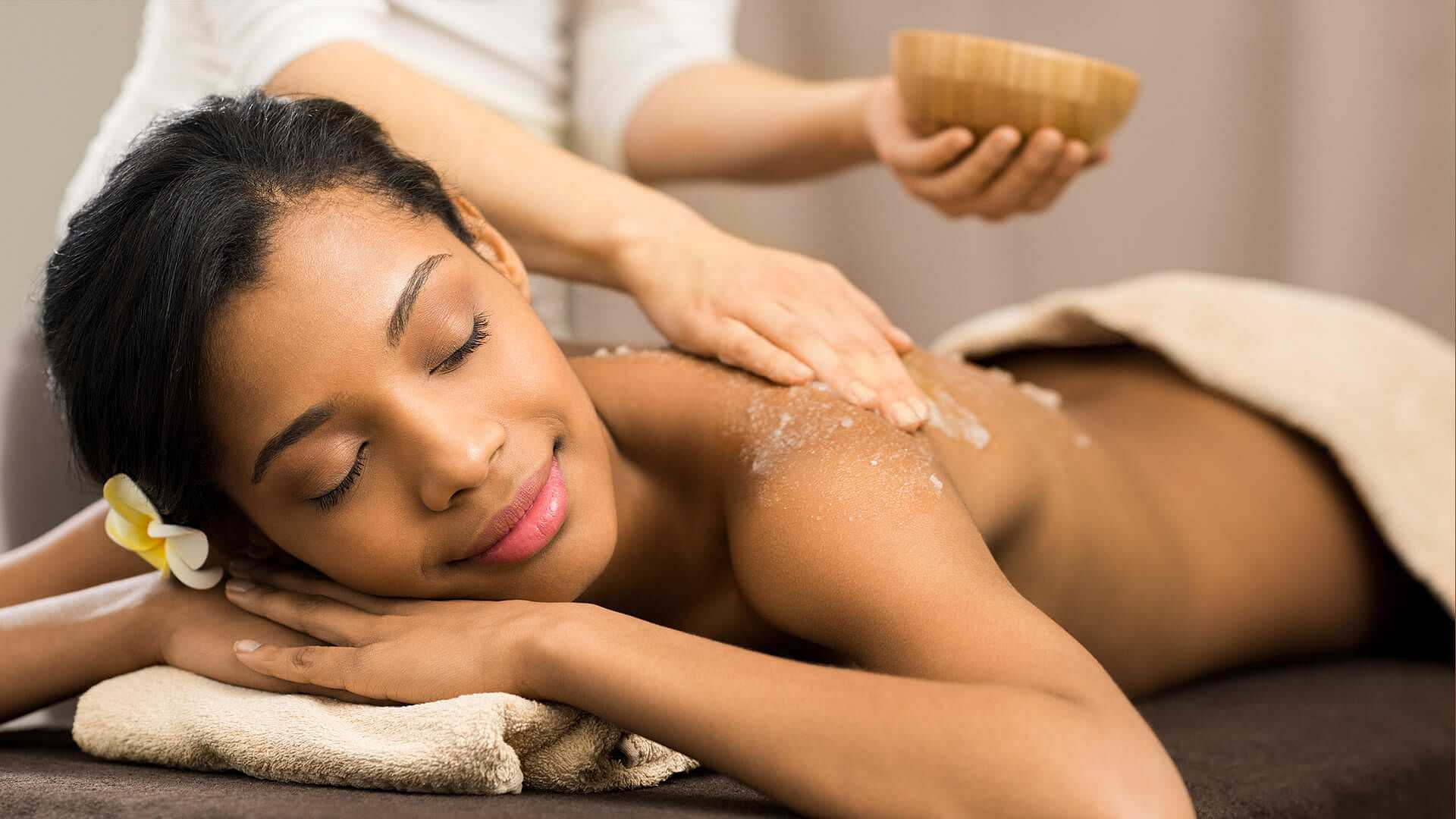 Woman receiving a relaxing back massage in a spa setting, eyes closed, with a towel draped over her.