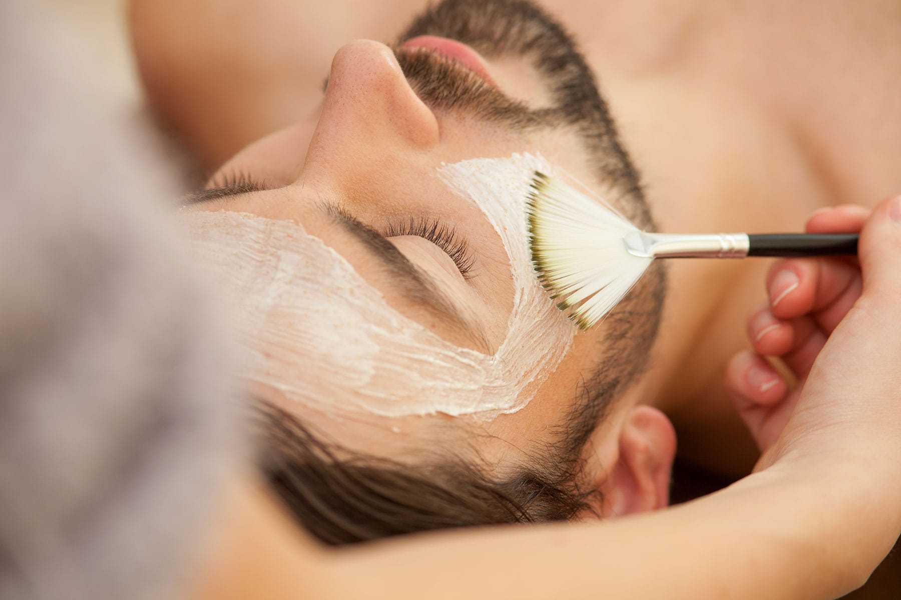 Man receiving a facial treatment with a brush application.