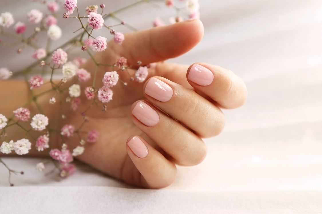 Hand with pink manicured nails holding delicate baby's breath flowers.