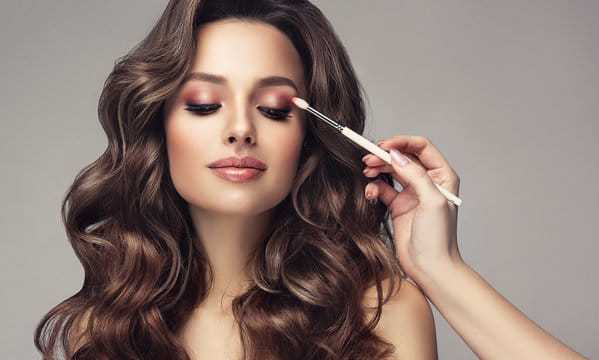 Woman getting eye makeup applied with a brush, showcasing a glam look.
