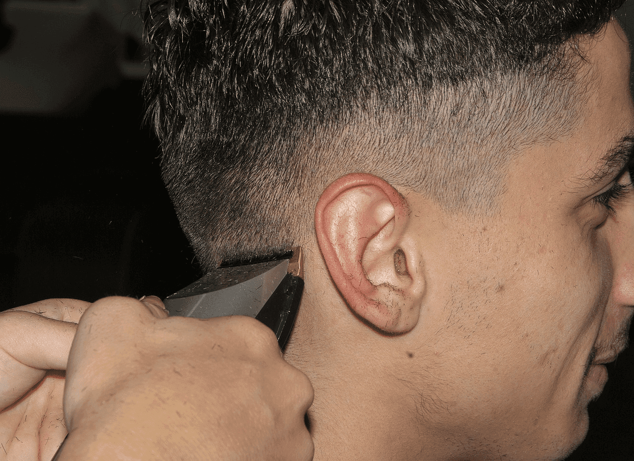 Man receives a haircut with clippers, showing close-up of hair and skin fade.