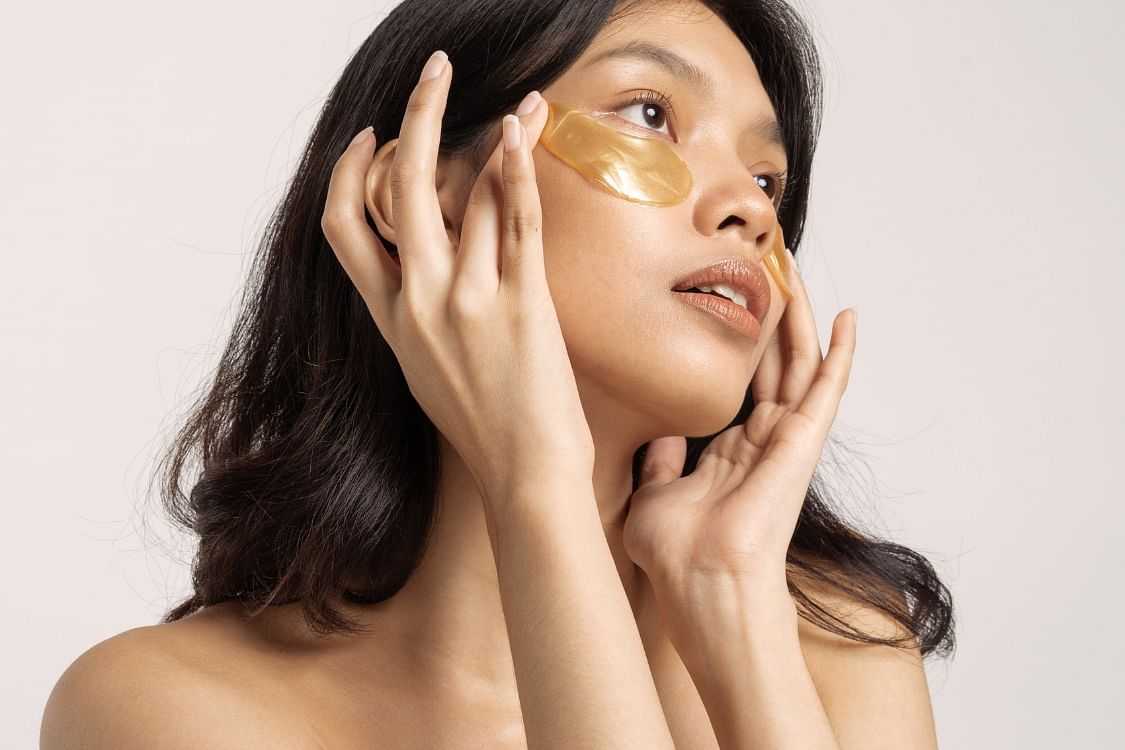 Woman applying gold under-eye skincare patches.